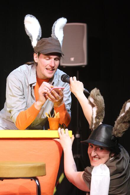 B&uuml;hnenfoto: Hoppel Lodengr&uuml;n (gespielt von Mark Roberts) singt vor sich hin und Ren&eacute; Ohrenschmalz (gespielt von Manuela H&ouml;rr) h&auml;lt ihm heimlich ein Mikrofon vor die Nase und klaut so seine Stimme.